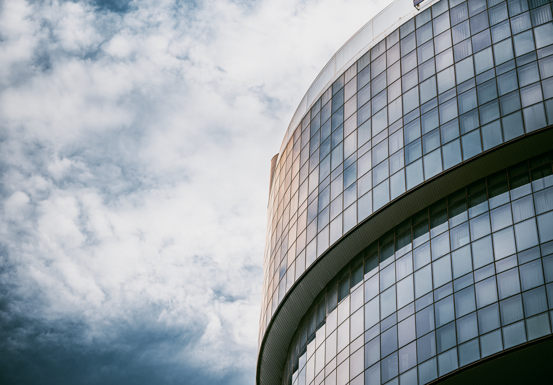 A sleek, modern glass building in Bangkok under a dramatic cloudy sky.