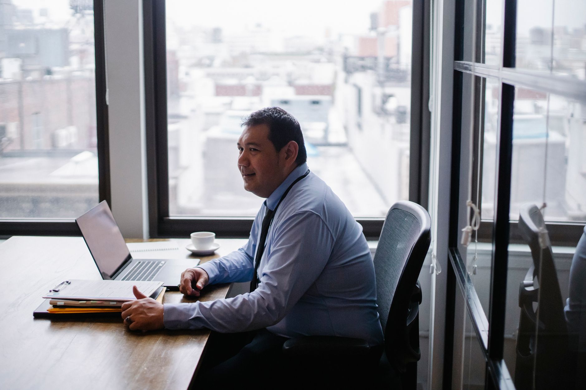 High angle side view of smiling ethnic businessman sitting in armchair at table with netbook and documents