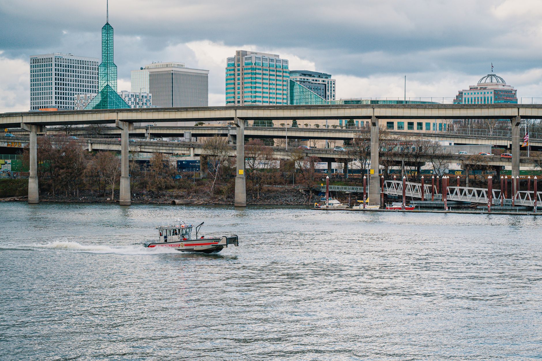 Stunning view of Portland's skyline featuring a riverboat under a modern bridge on a cloudy day.