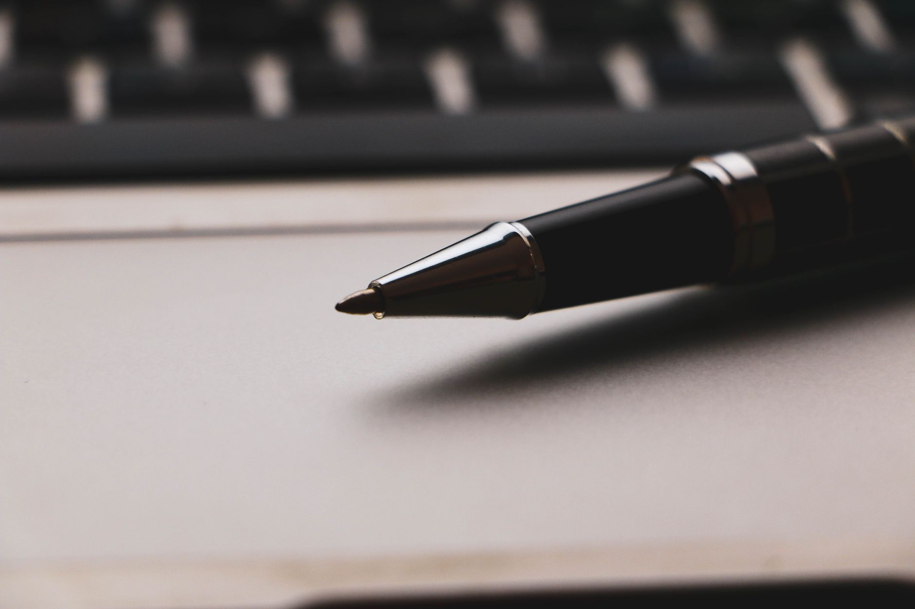 A focused close-up of a ballpoint pen resting on a laptop, emphasizing productivity.