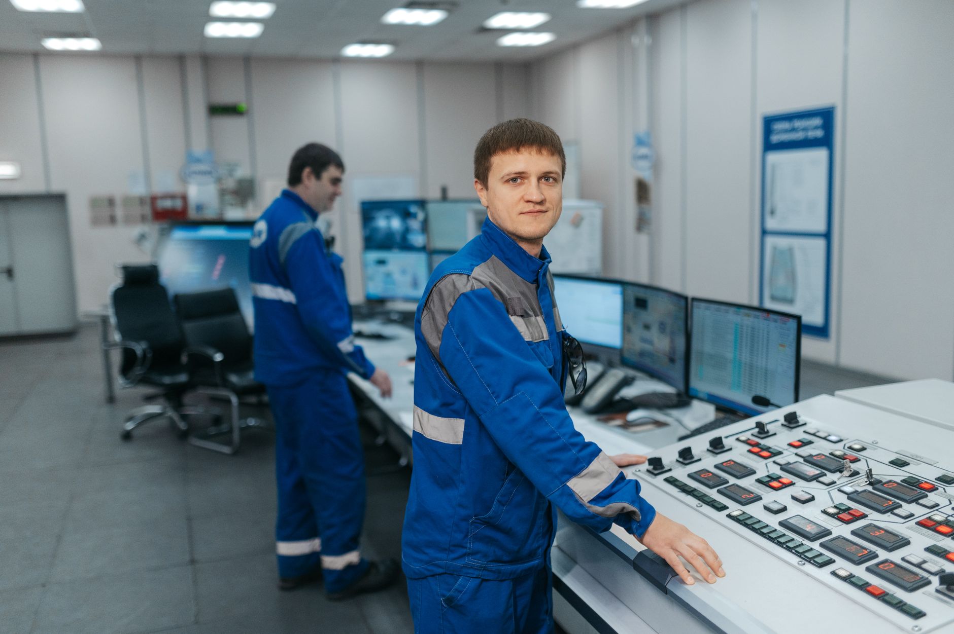 Two technicians operating machinery in a modern control room. Industrial setting with advanced equipment.
