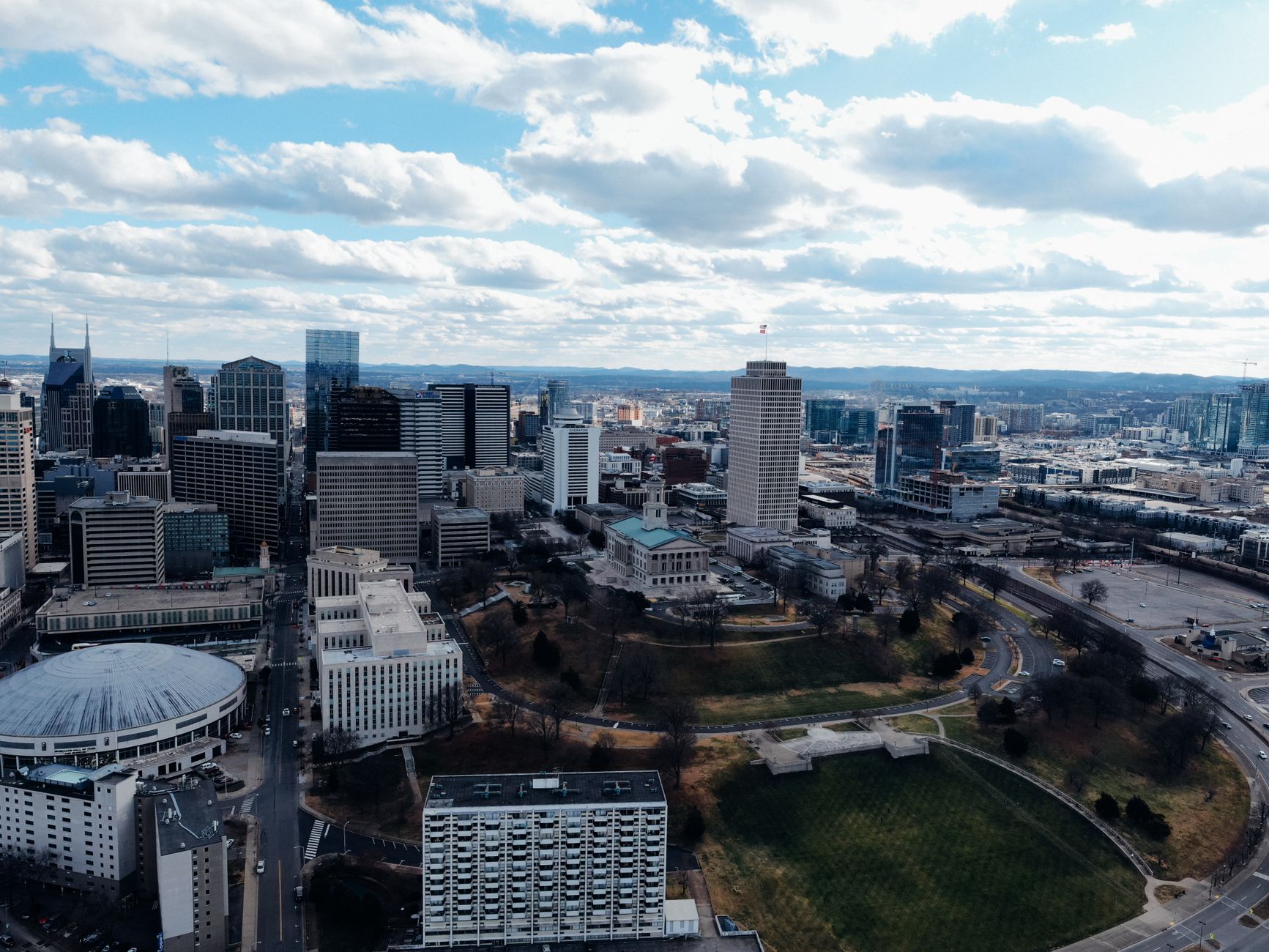 Drone view of modern multistory building exteriors and trees under cloudy sky in town