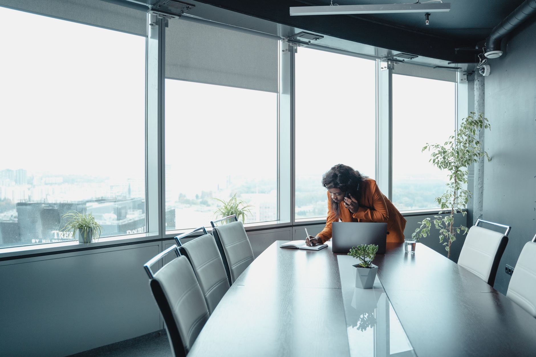 Businesswoman in a modern office writing while talking on the phone.