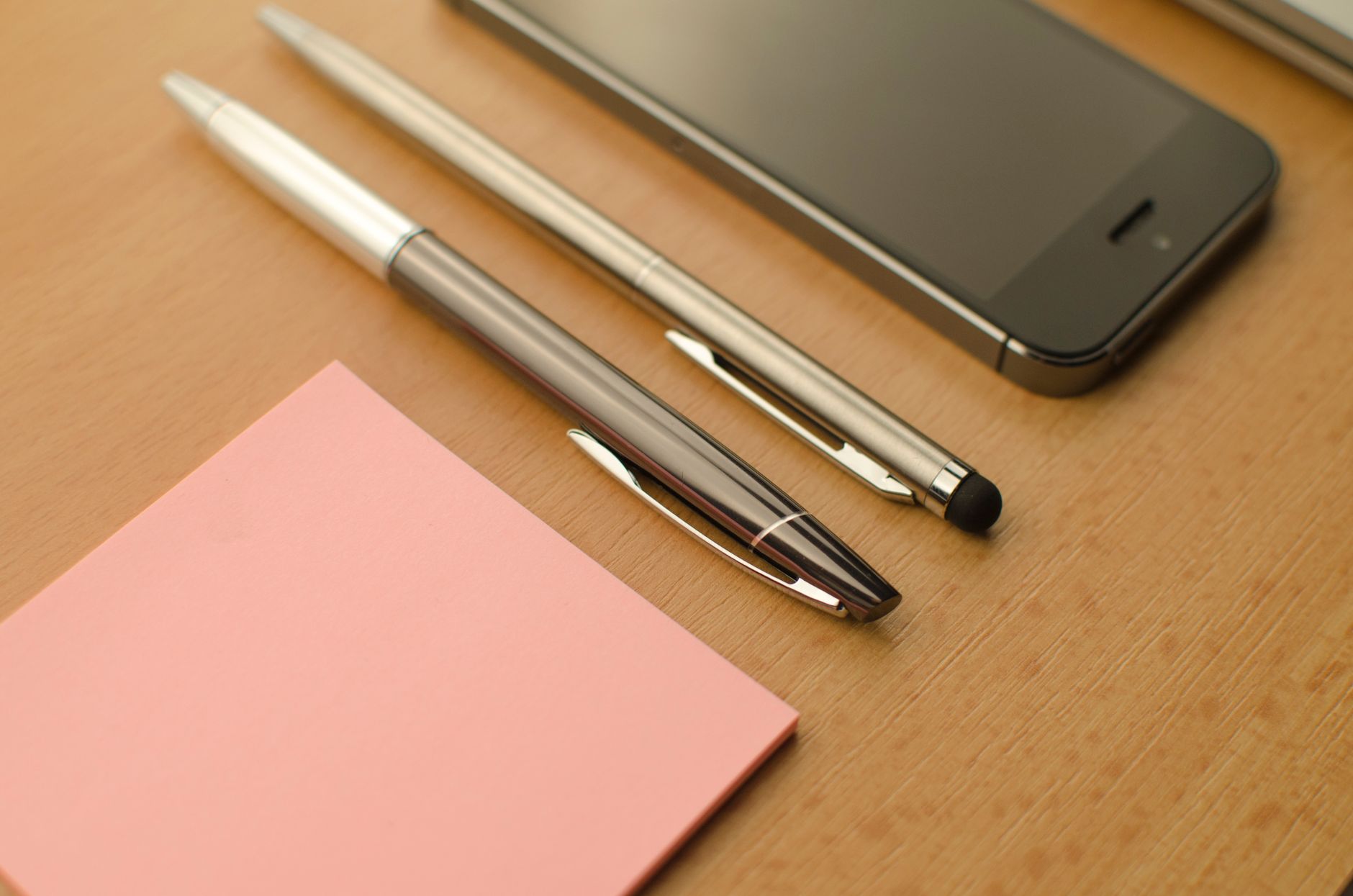 Stylish workspace featuring a smartphone, pens, and a notepad on a wooden desk.