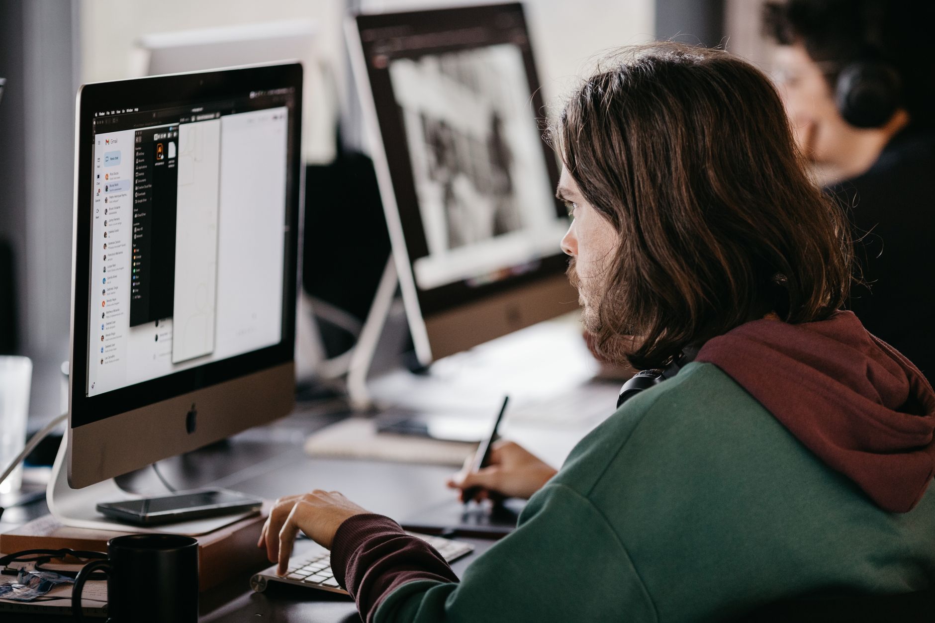Person in a hoodie working at a desktop computer in an office setting, focused and engaged.