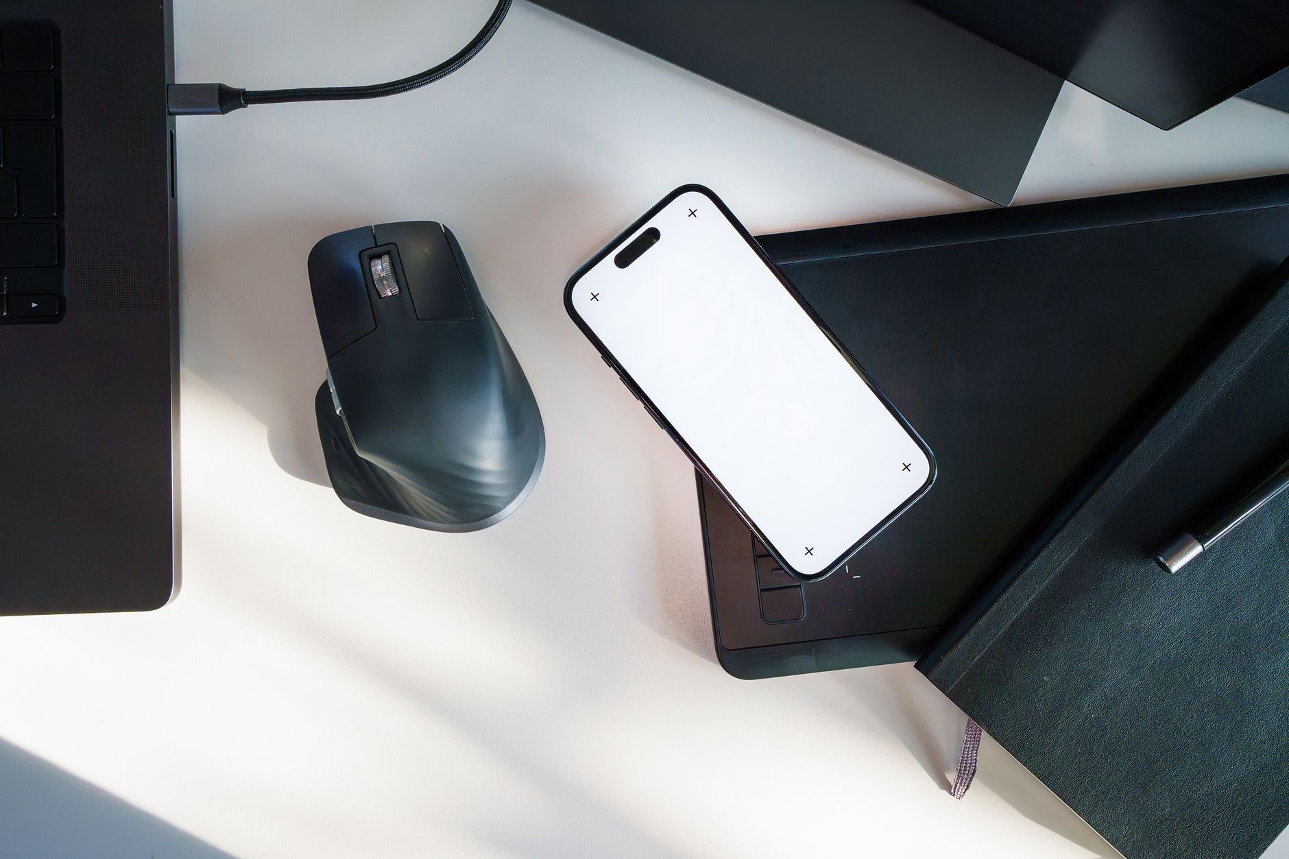 Top-down view of a sleek desk setup featuring a laptop, smartphone, wireless mouse, and notebook.