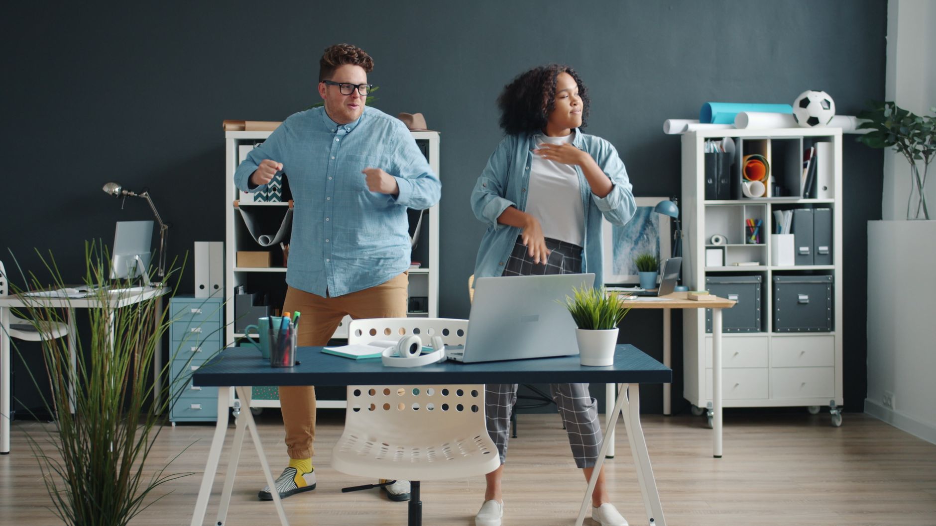 Two colleagues dancing in a modern office, enjoying a break from work.