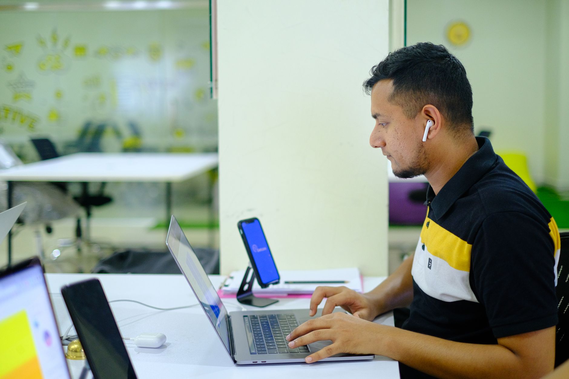 Asian man using laptop in a modern Sylhet office, working with earphones on.