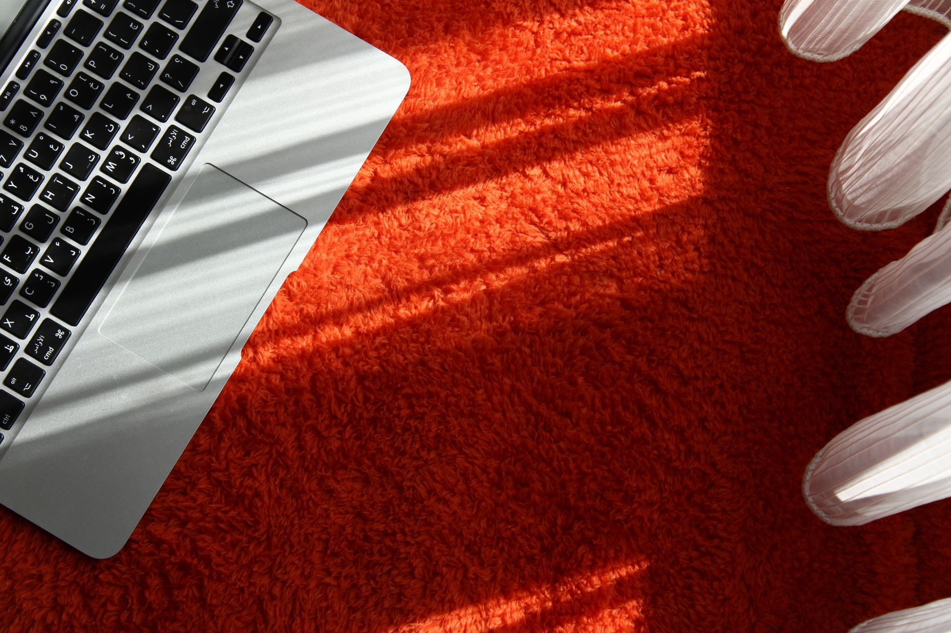 A close-up of a laptop on an orange carpet with sunlight casting shadows, symbolizing technology and creativity.