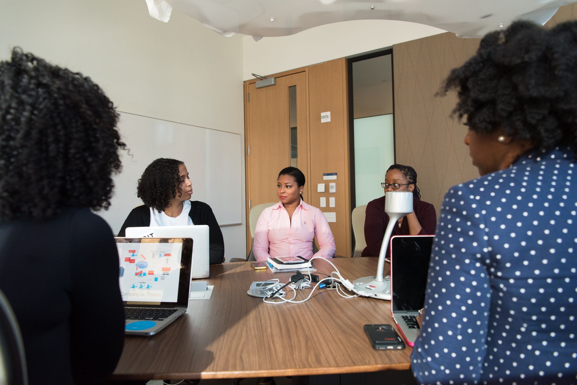 Diverse team of adults collaborating in a meeting room with laptops and documents on the table.