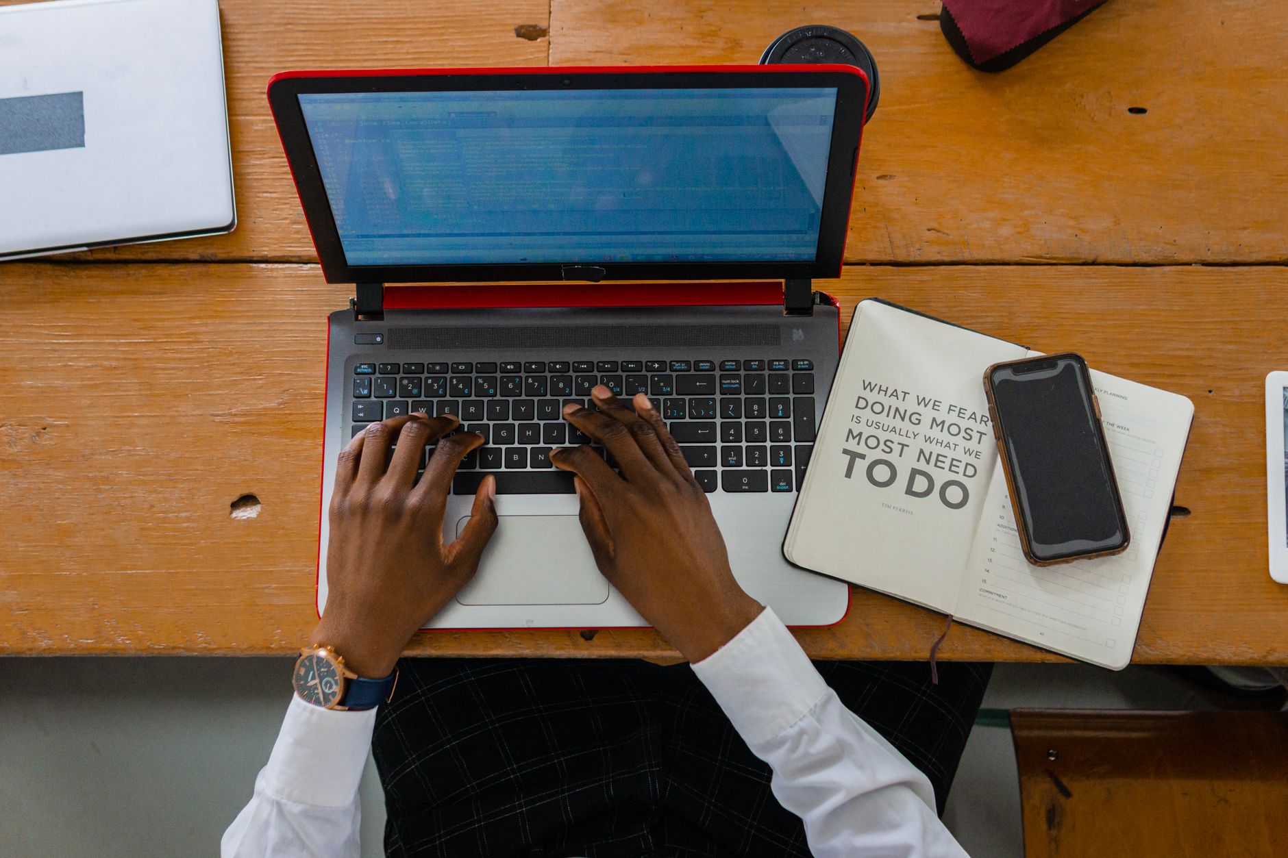 Person typing on a laptop with a notebook and smartphone on a wooden desk. Ideal for business or work themes.