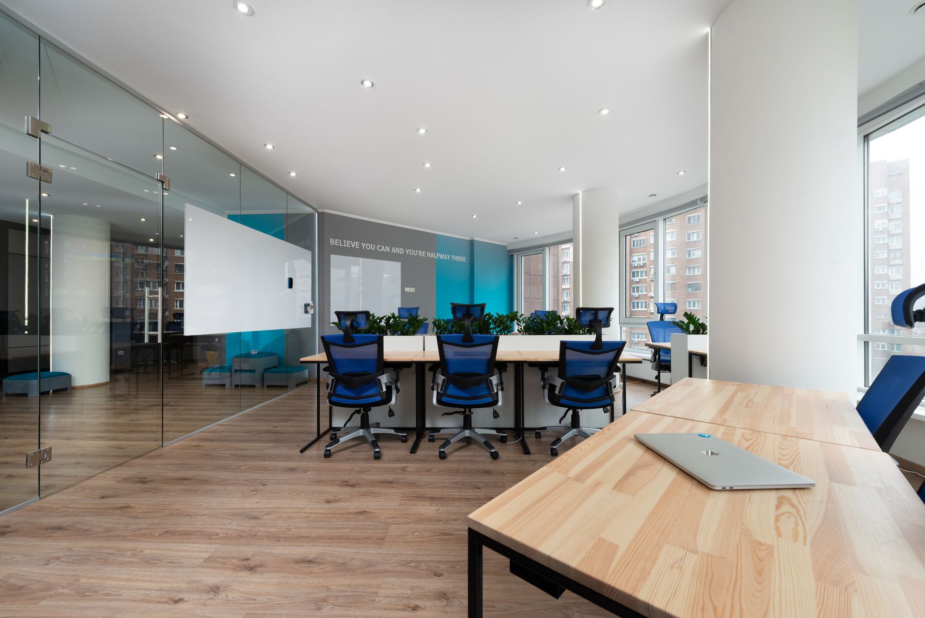 Blue armchairs at table near green plants placed in light boardroom with modern laptop and window in stylish office building