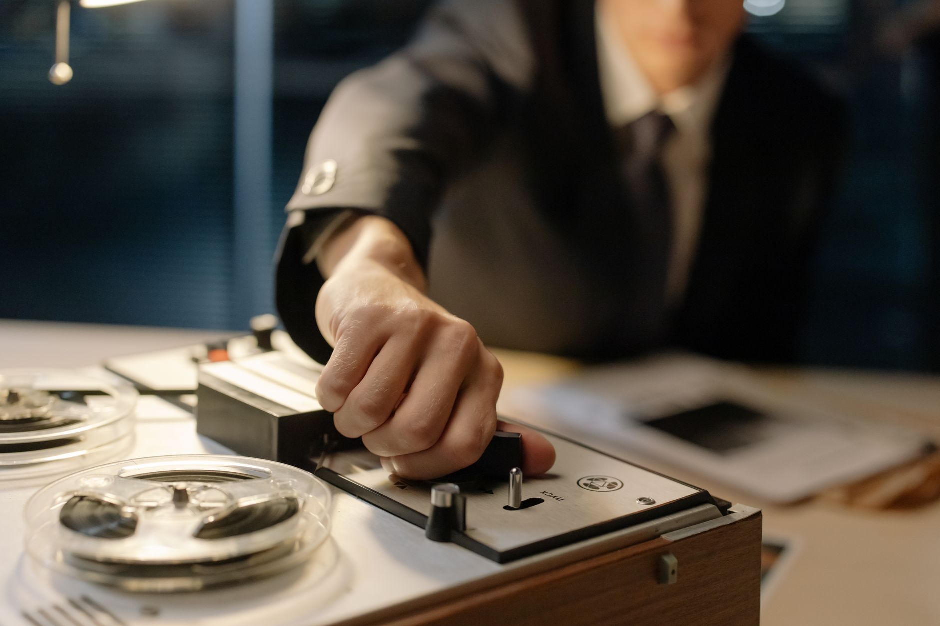 A suited man operates a retro tape recorder, evoking a classic interrogation scene.