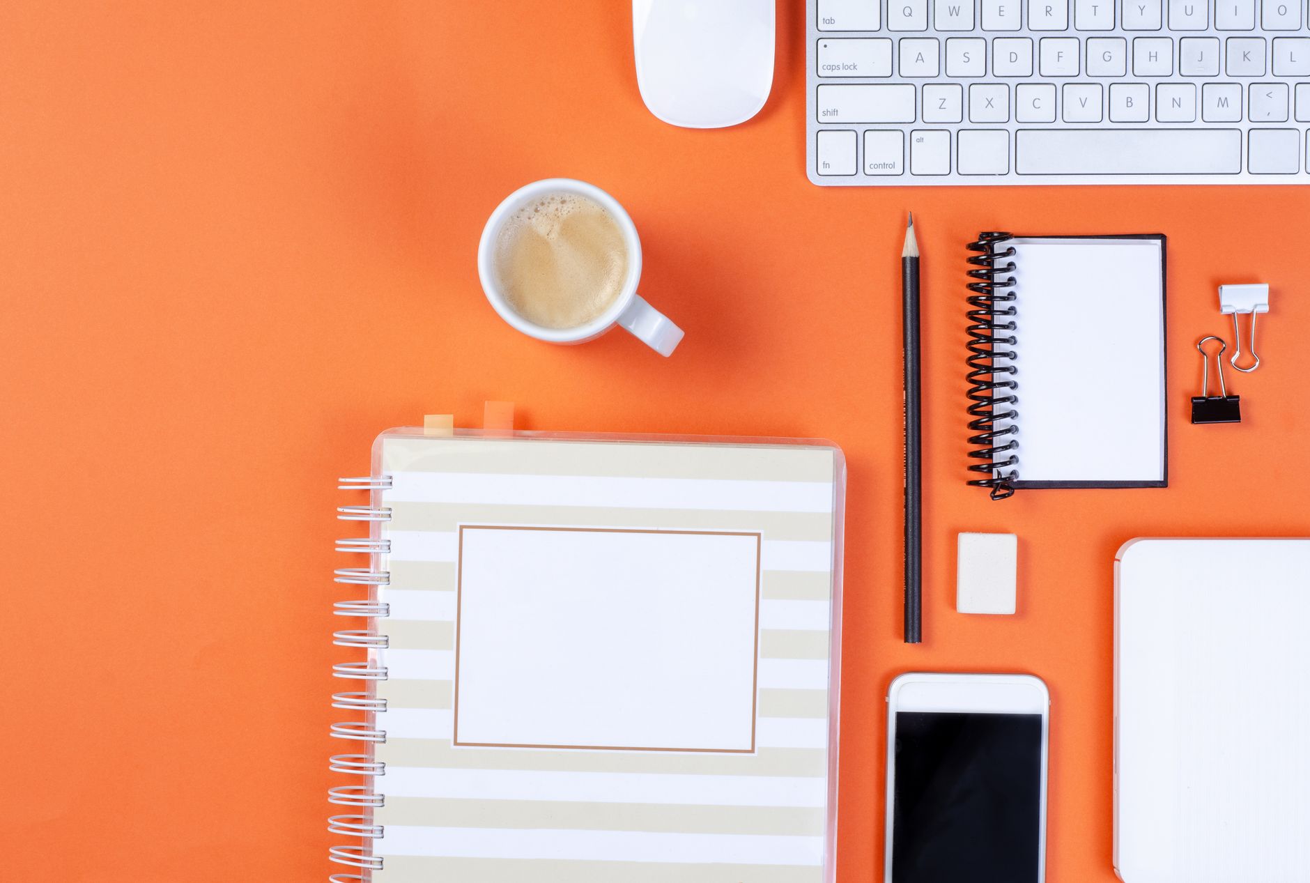 Flat lay of office items on an orange background including keyboard, coffee, and smartphone.