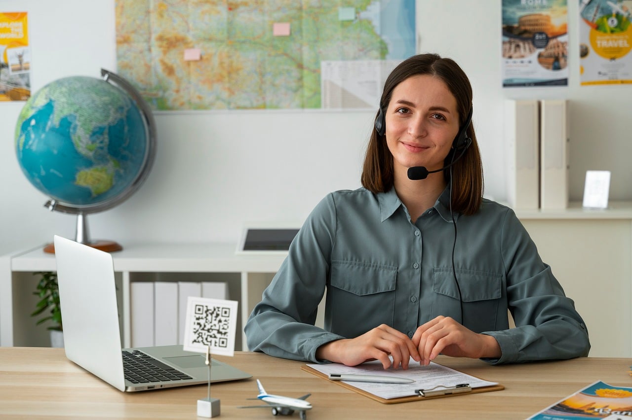 travel agency, travel agent, woman, headset microphone, laptop, globe, world map, travel poster, desk, work environment, office interior, international travel, qr code, airplane, documents, planner, smile, professional, young adult, communication
