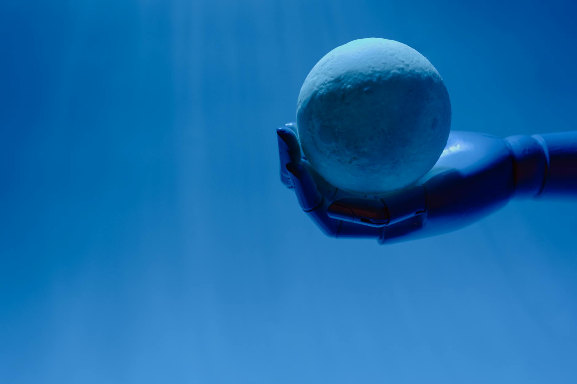 A robotic hand holds a glowing celestial sphere against a blue background, evoking a futuristic theme.