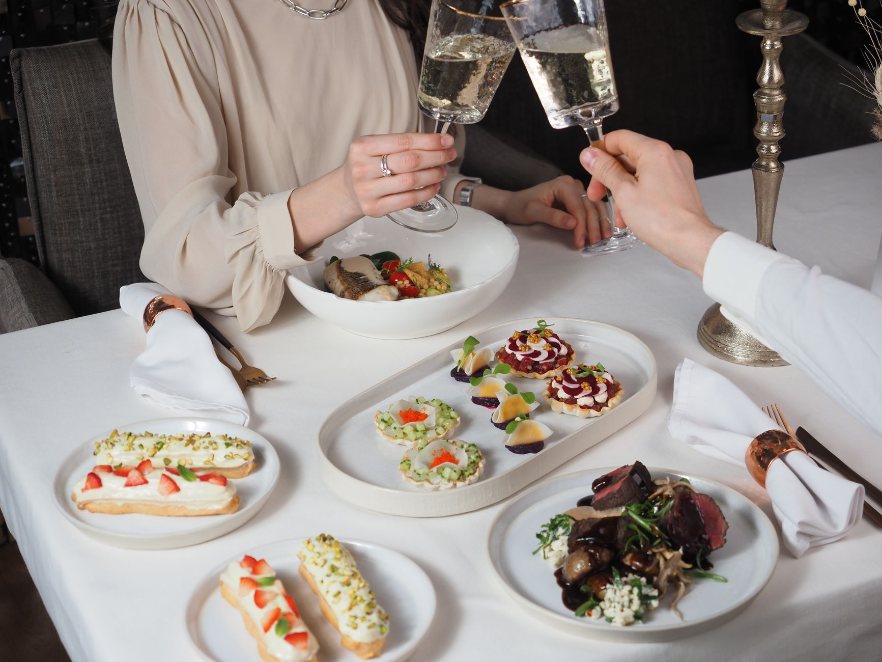 Elegant dining scene with a couple toasting with champagne over gourmet dishes.