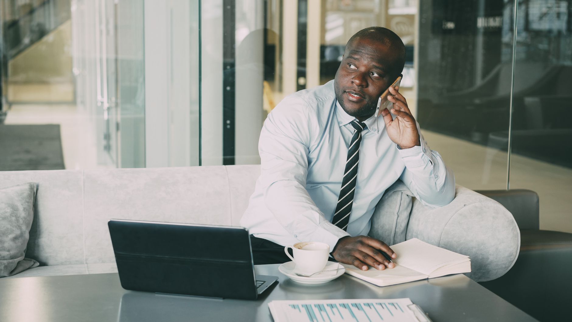 Adult businessman in office lounge using laptop and smartphone with coffee.