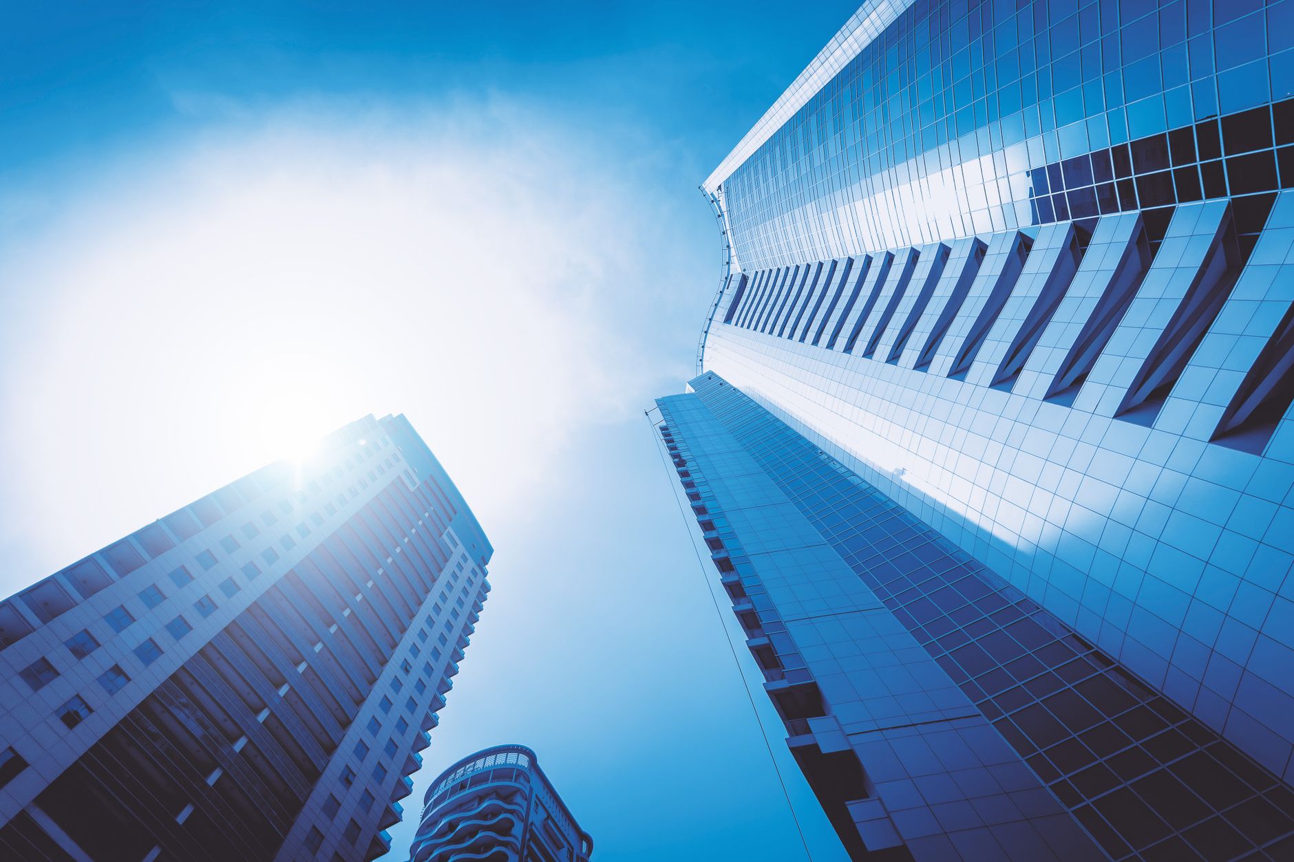 Low angle view of futuristic skyscrapers in a cityscape against a bright blue sky.