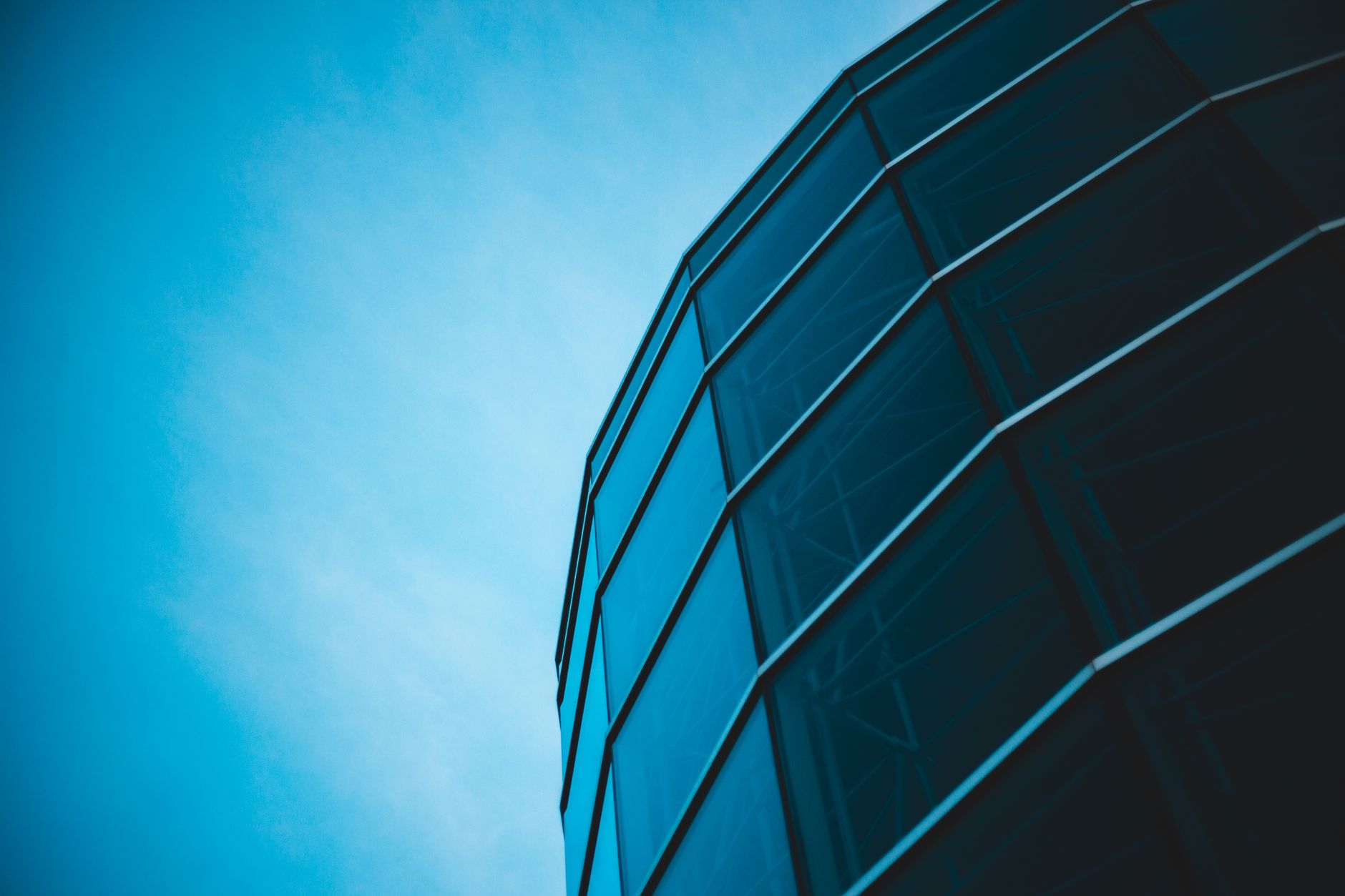 Low-angle view of modern glass architecture set against a bright blue sky, offering a minimalist and sleek design perspective.