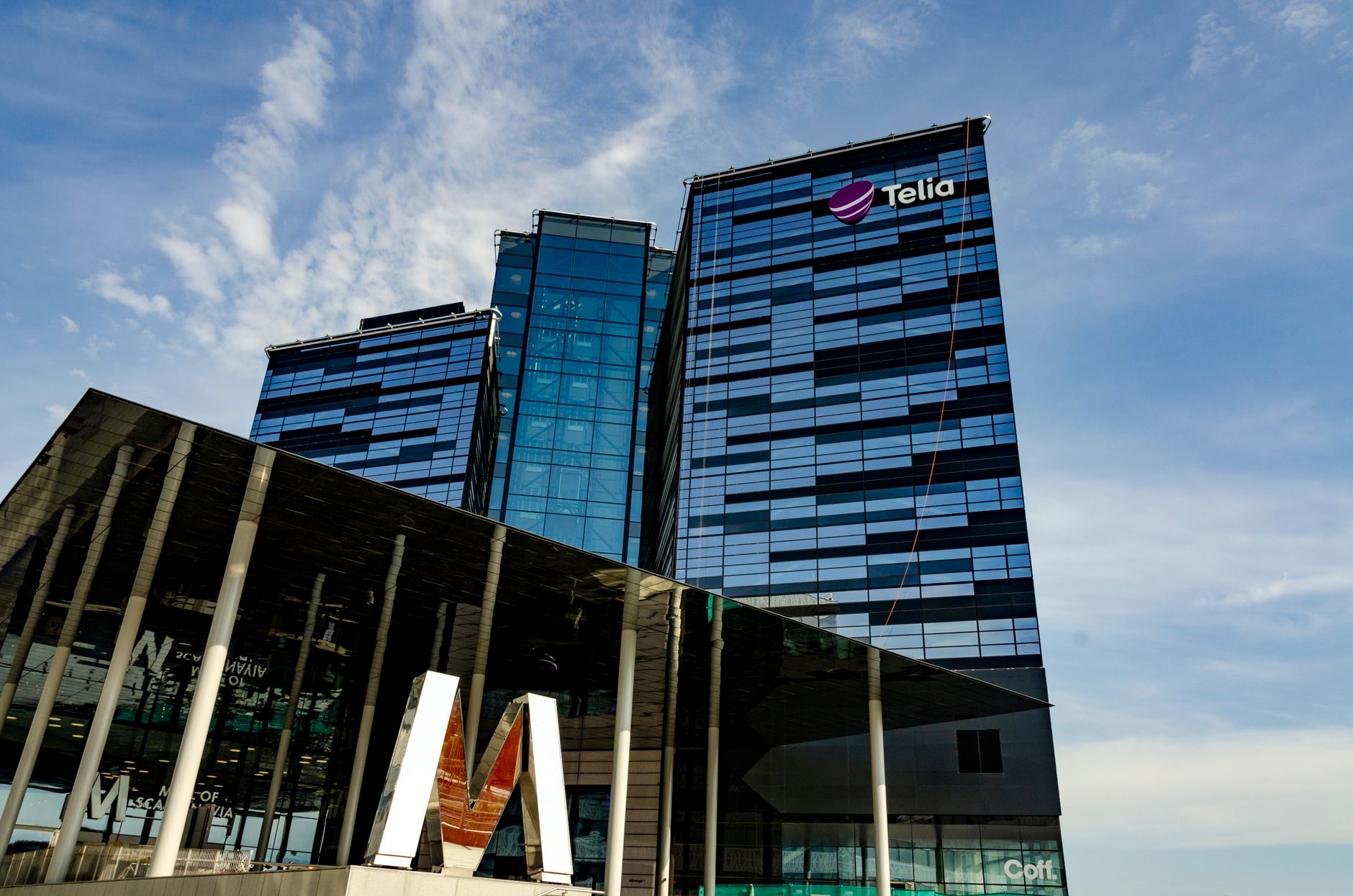 Modern glass office building in Stockholm with Telia logo on a sunny day.