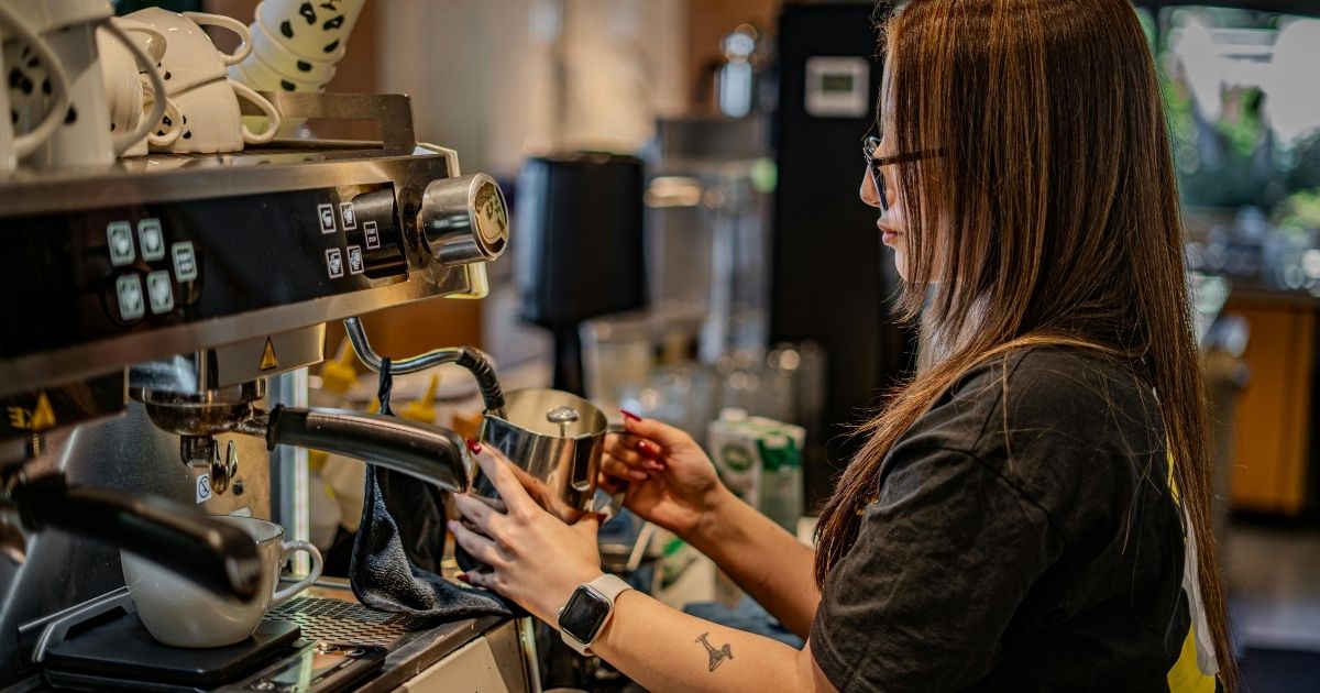A woman preparing a espresso coffee in a coffee service machine - Busy Bean Coffee