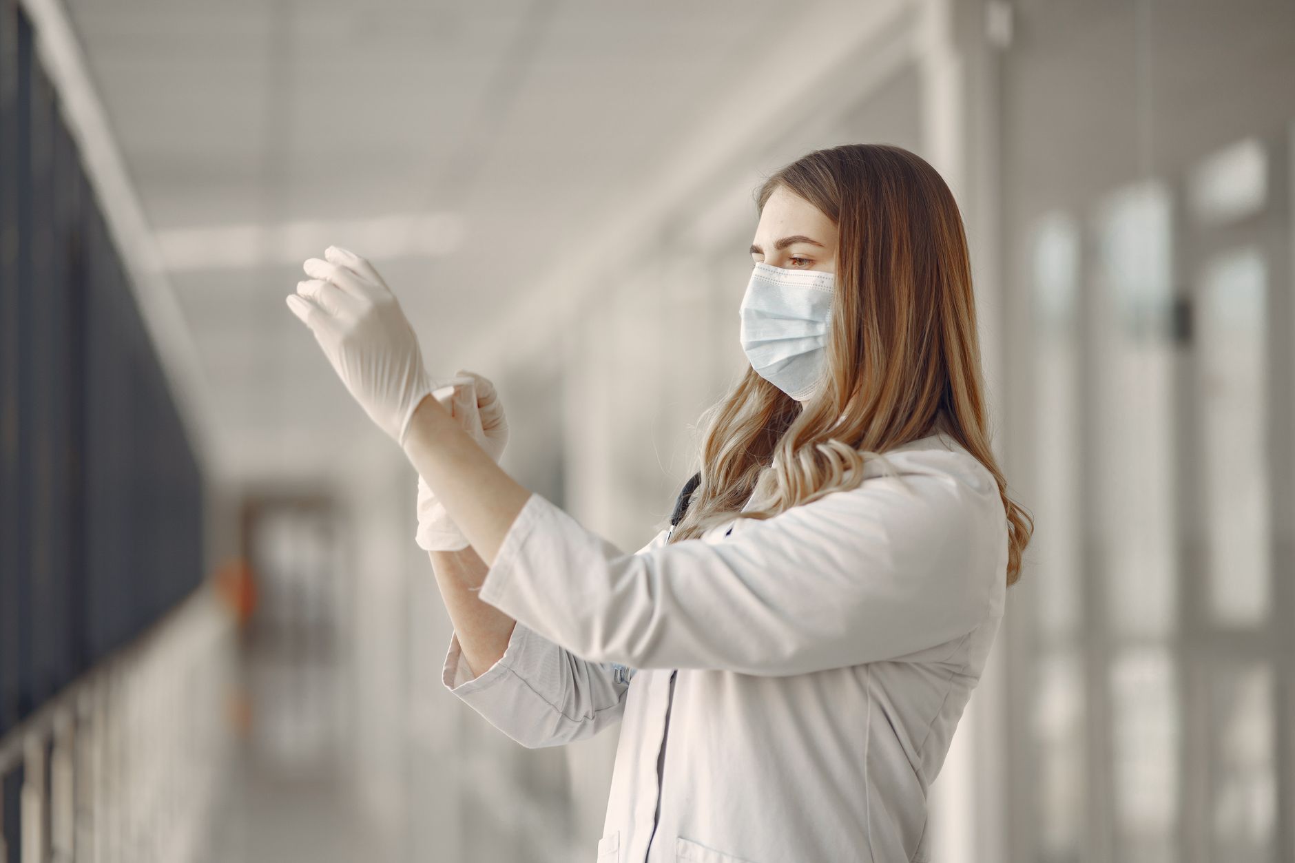 A female doctor adjusts her gloves in a hospital hallway, emphasizing safety and professionalism.