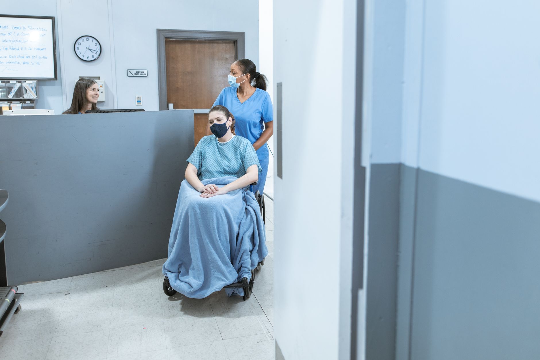 Nurse assisting a patient in a wheelchair at a medical facility reception.