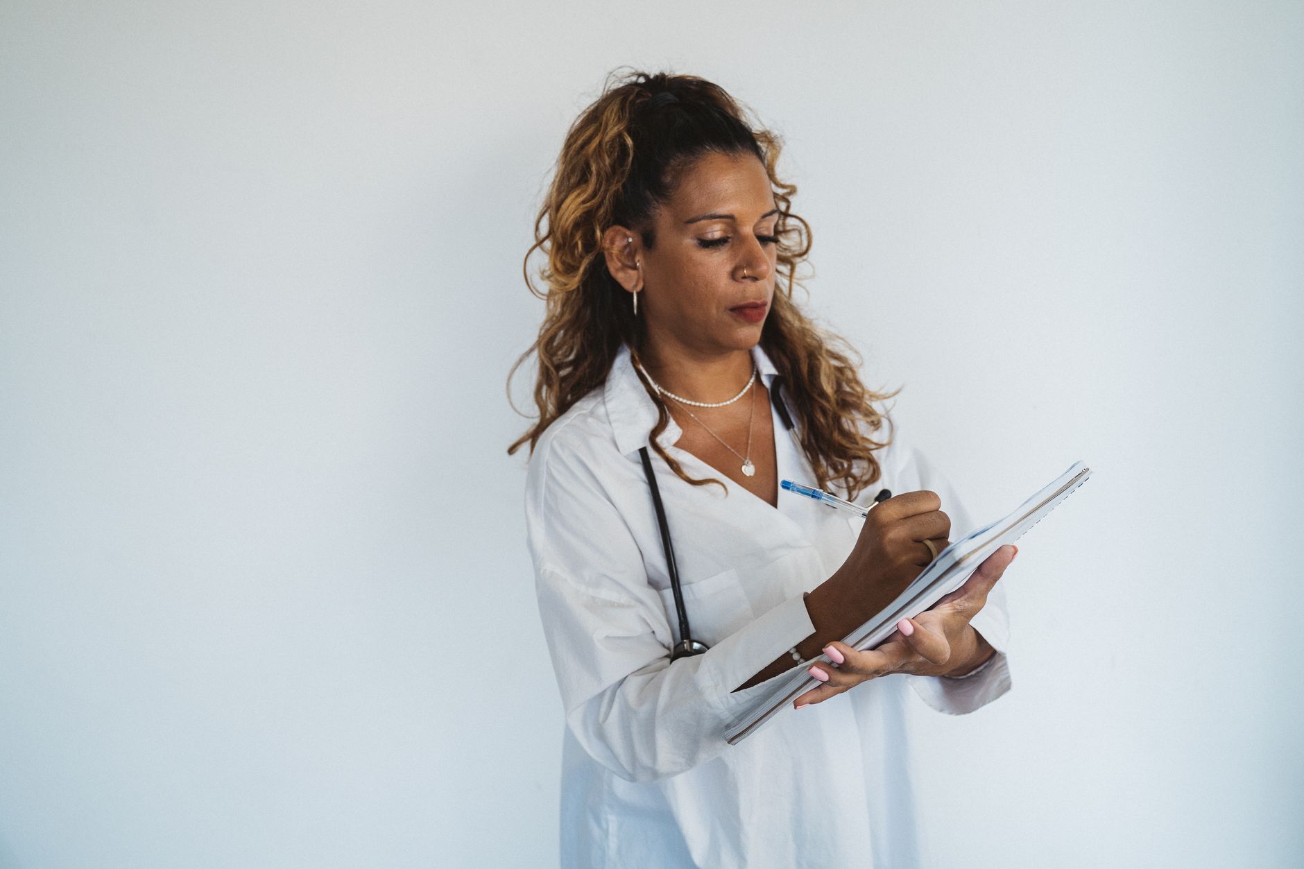 Professional female doctor writing notes with a pen on a notepad against a white background.