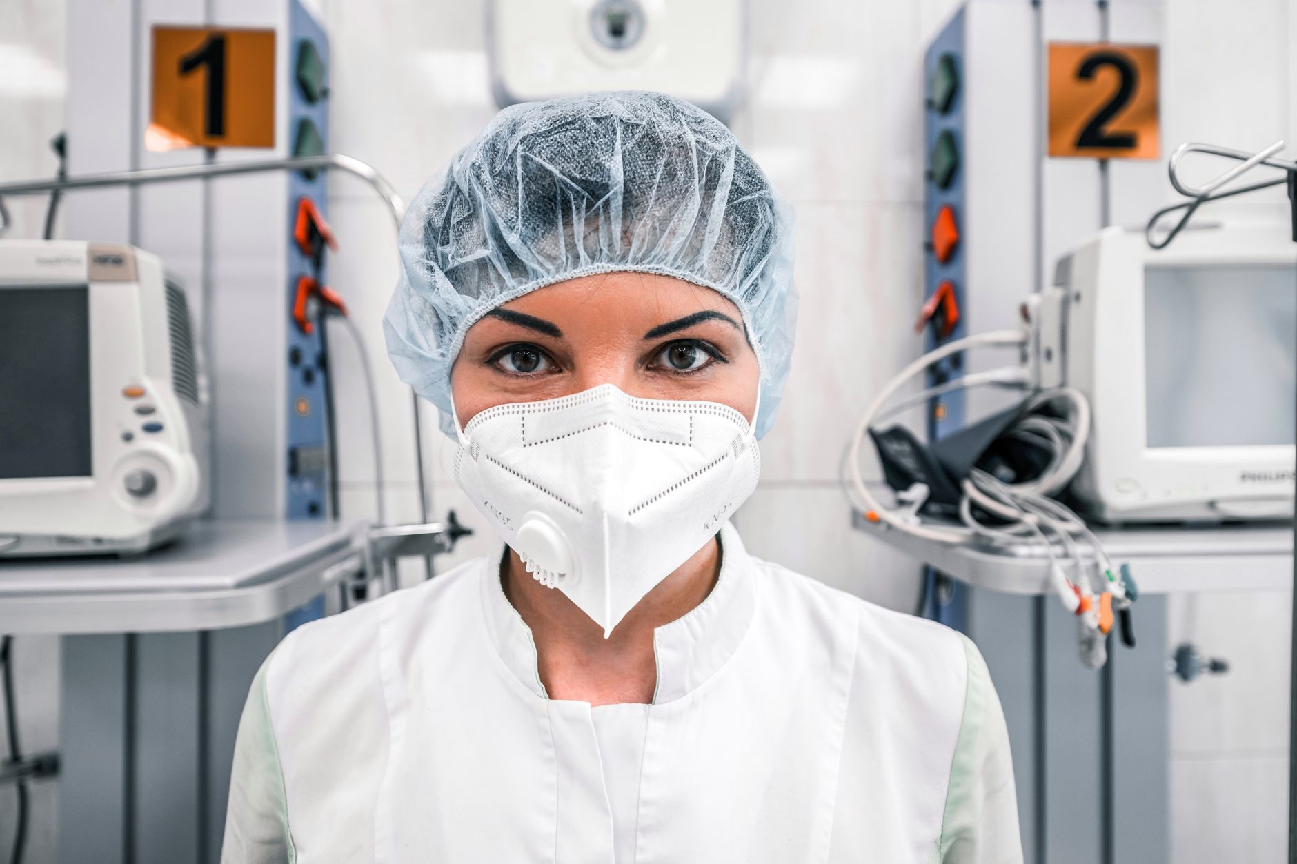 Female healthcare worker in a hospital wearing a mask and surgical cap, standing confidently.