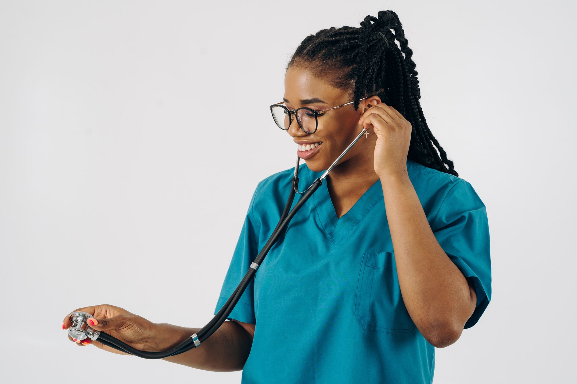 A black female doctor in blue scrubs, smiling while holding a stethoscope on a white background.