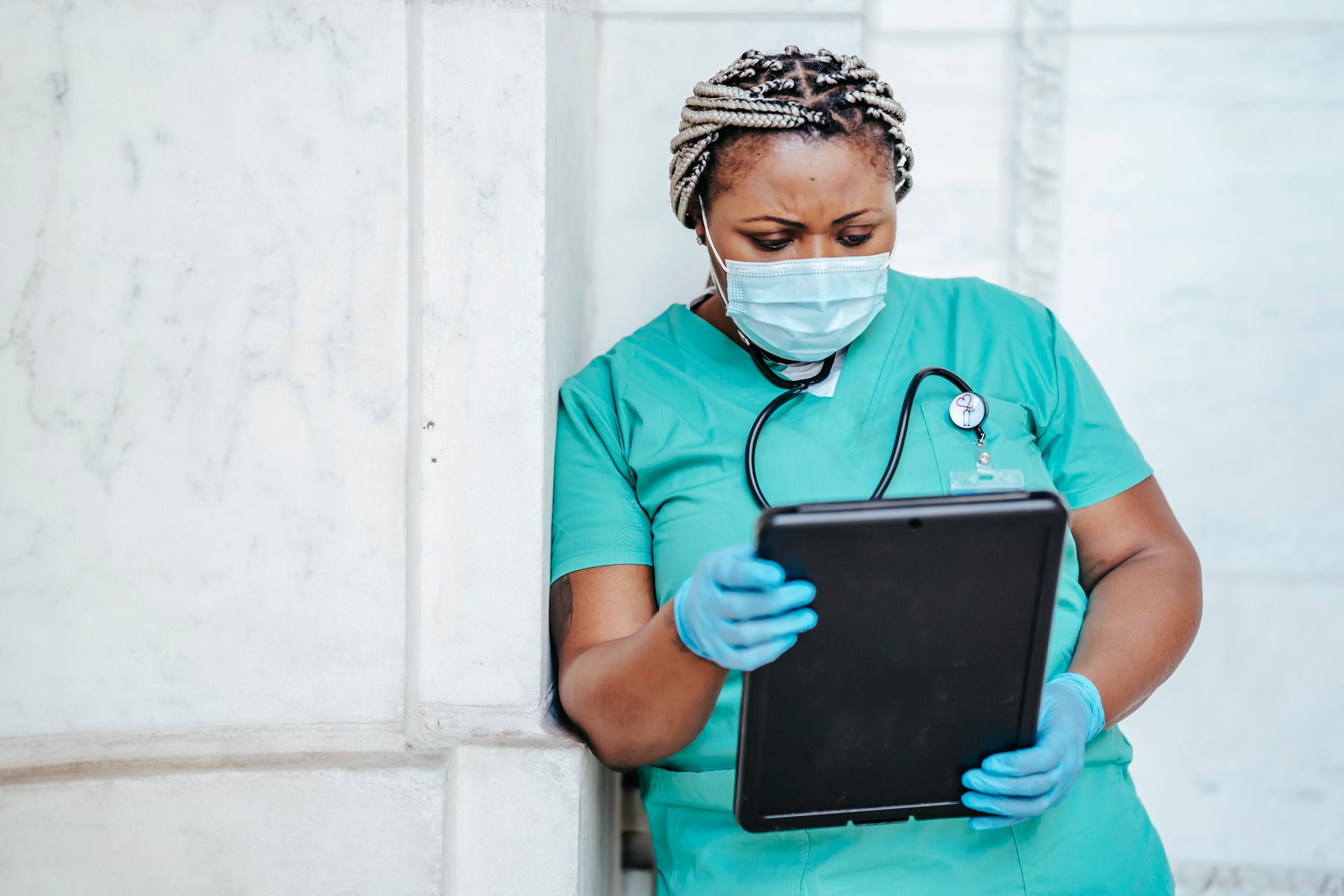 Concentrated African American female doctor in uniform and protective mask looking through documents in folder