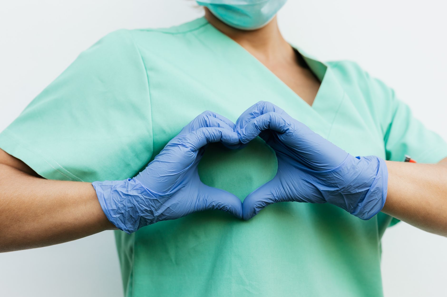 Nurse in blue gloves making a heart shape with hands, symbolizing compassion and care.