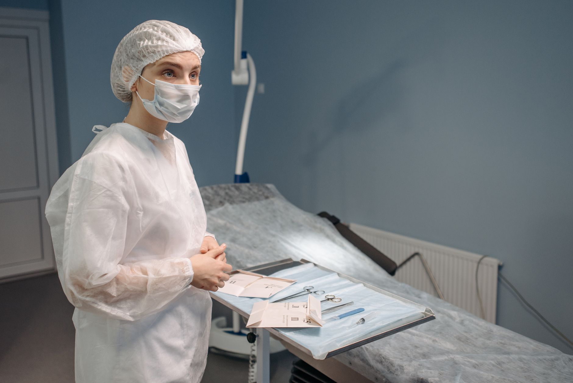 Medical professional in protective gear preparing surgical tools in a hospital setting.