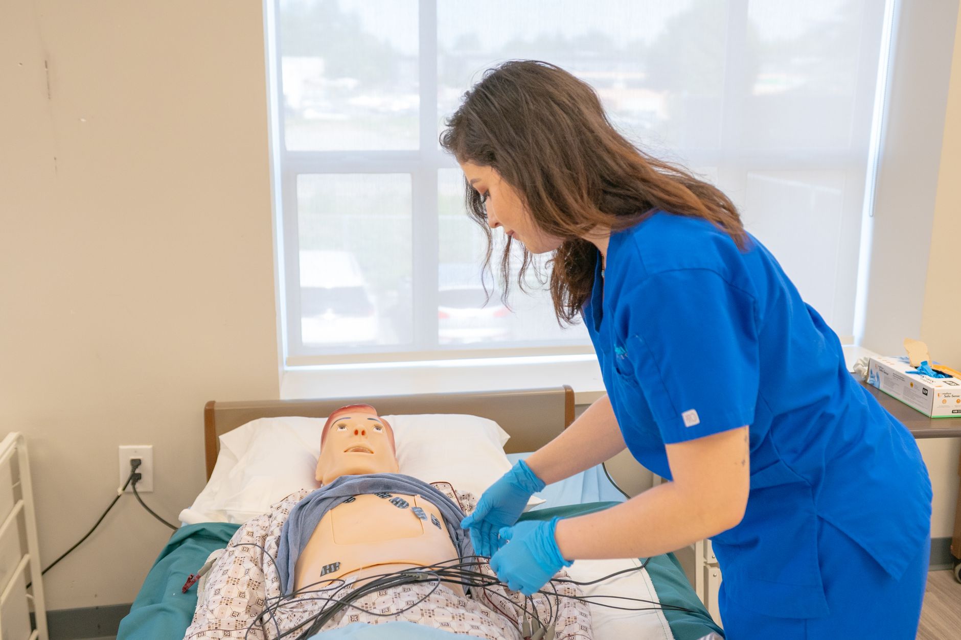 Nursing student practicing medical procedures on a mannequin in a clinical lab setting.