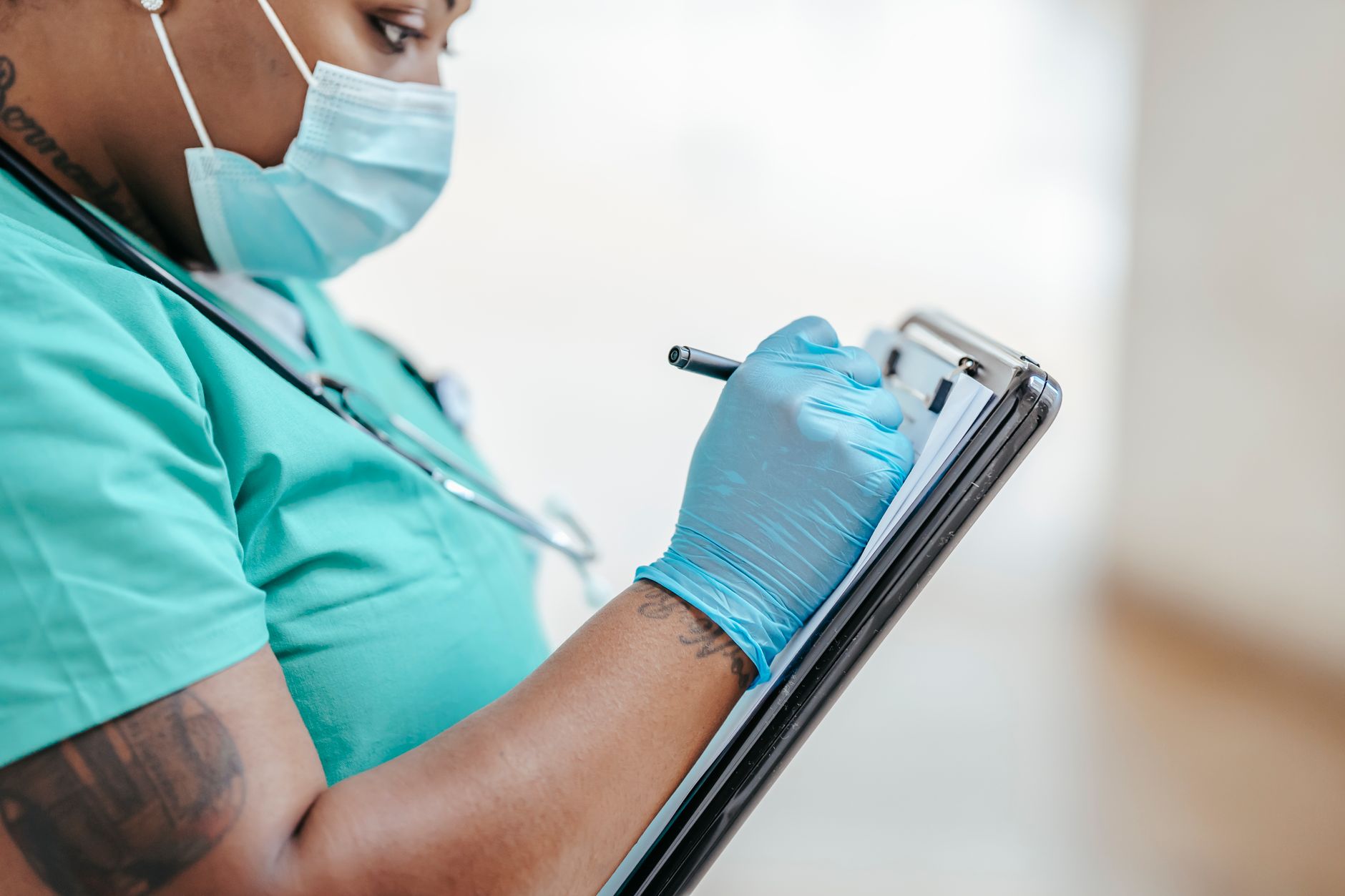 Side view of crop mature black female medic in uniform taking notes on paper document on clipboard