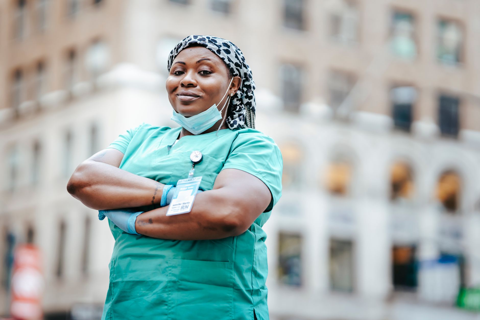 Low angle of confident African American nurse in gloves and mask standing with crossed arms and looking at camera
