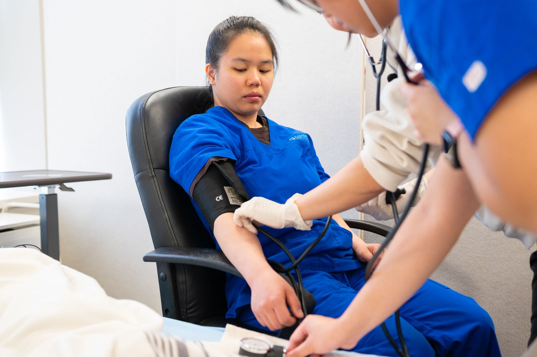 A nurse in blue scrubs checks a patient's blood pressure in a clinical setting.