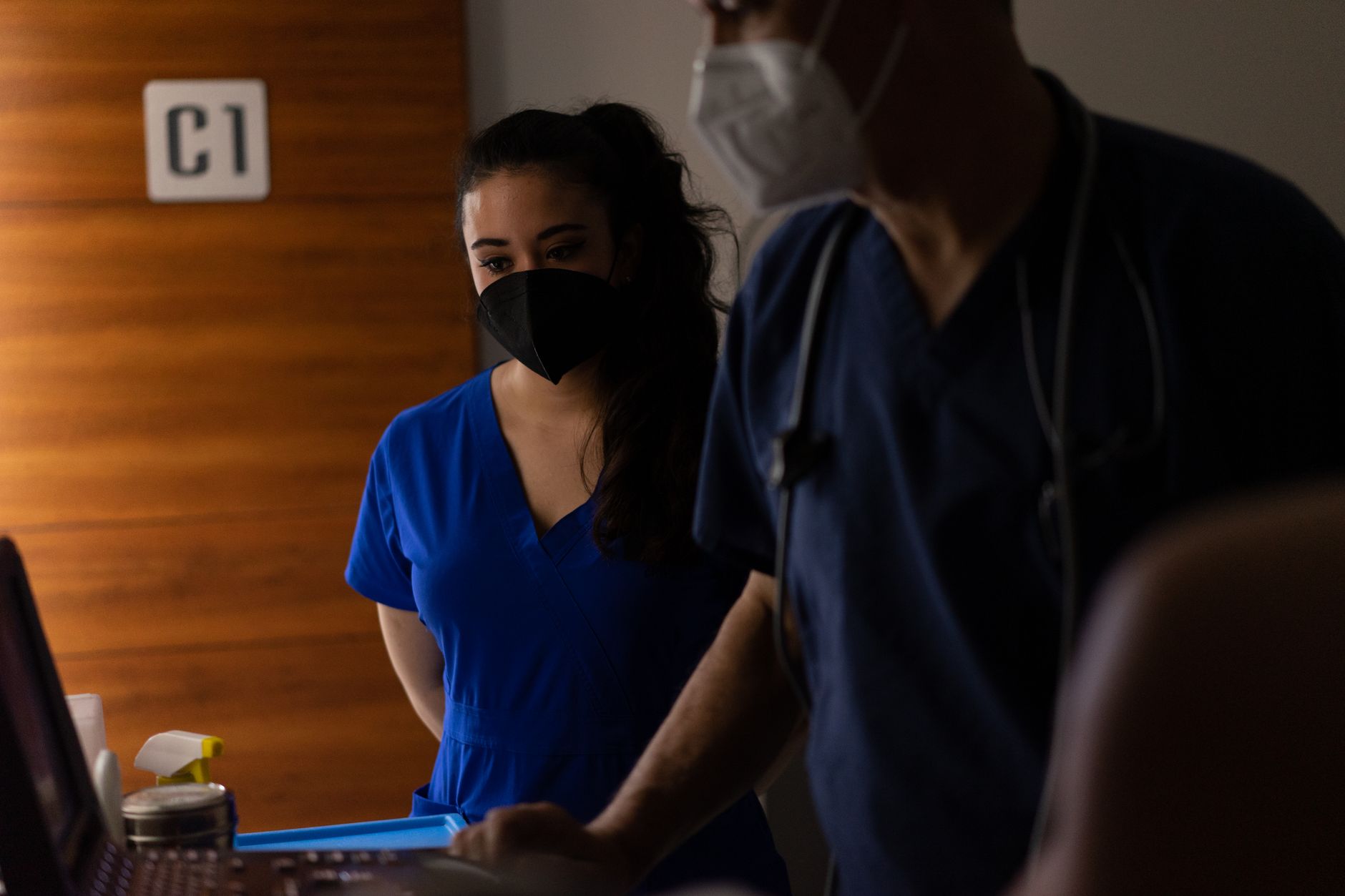 Doctors in scrubs and masks examining patient data in a hospital room.