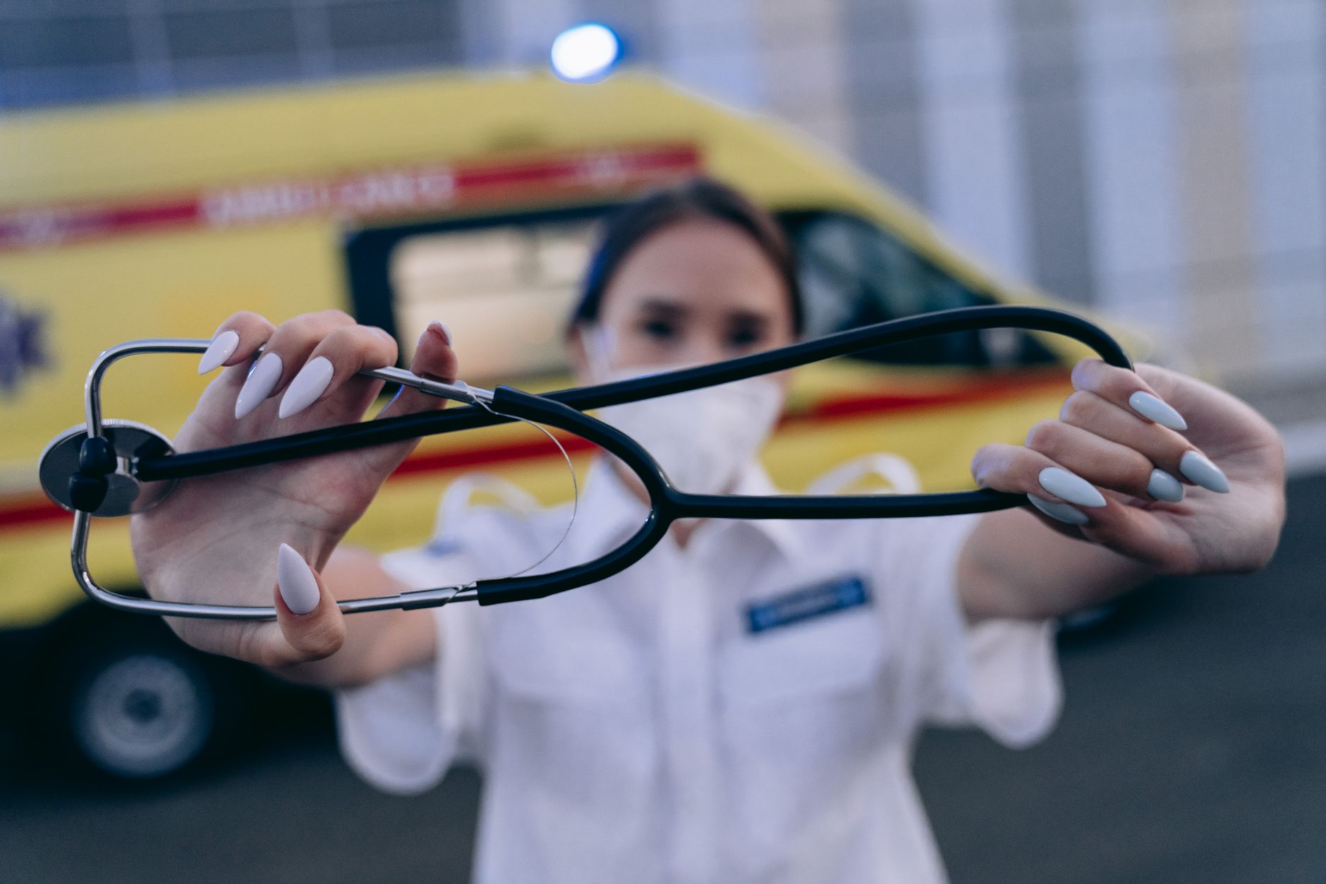 Close-up of a paramedic holding a stethoscope, with an ambulance in the background. Ideal for healthcare themes.