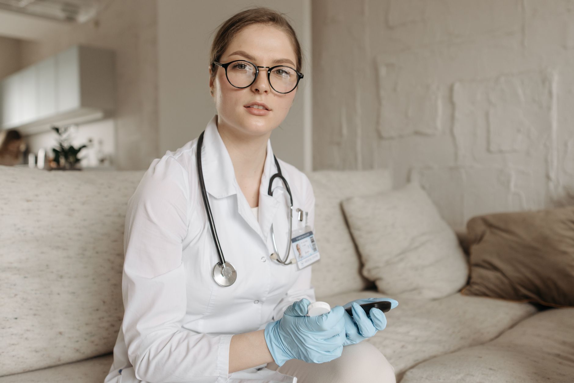 Female doctor with glucometer on a sofa, assessing blood sugar control indoors.