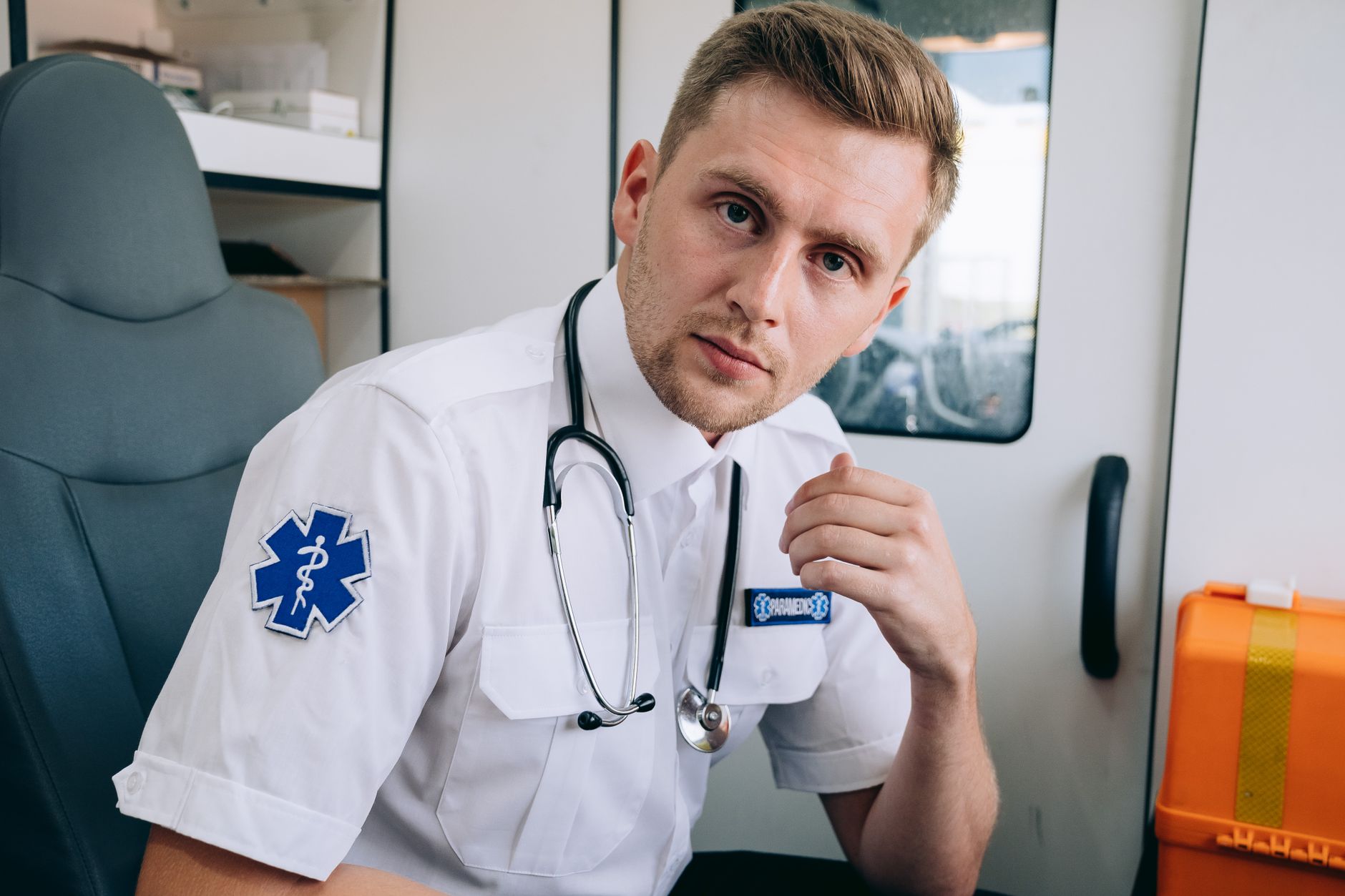A paramedic in uniform inside an ambulance, with a stethoscope, ready to assist.