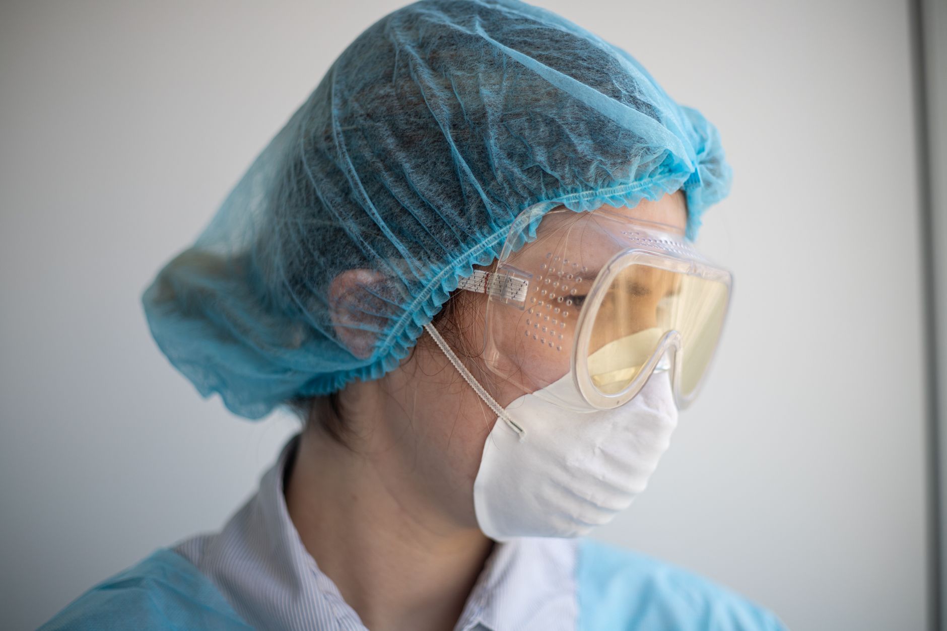 A healthcare worker in full PPE, including goggles and mask, focused on tasks.