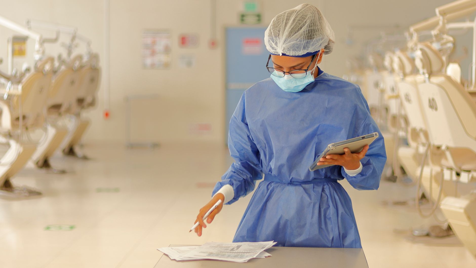 A healthcare professional in blue protective gear reviews documents in a medical clinic.