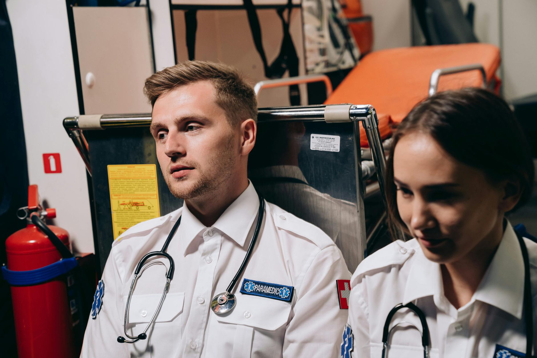 Two paramedics sitting in an ambulance, equipped with stethoscopes and emergency tools.