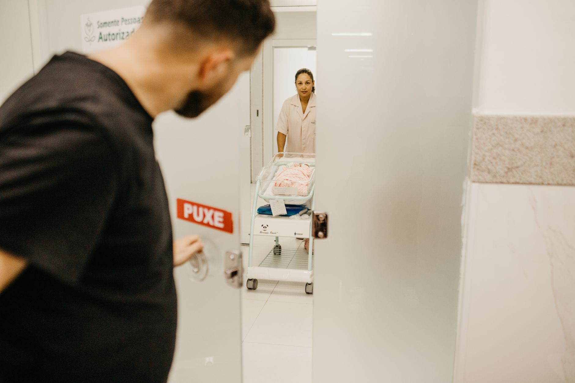 A man opens a door to see his newborn in a hospital room attended by a nurse.