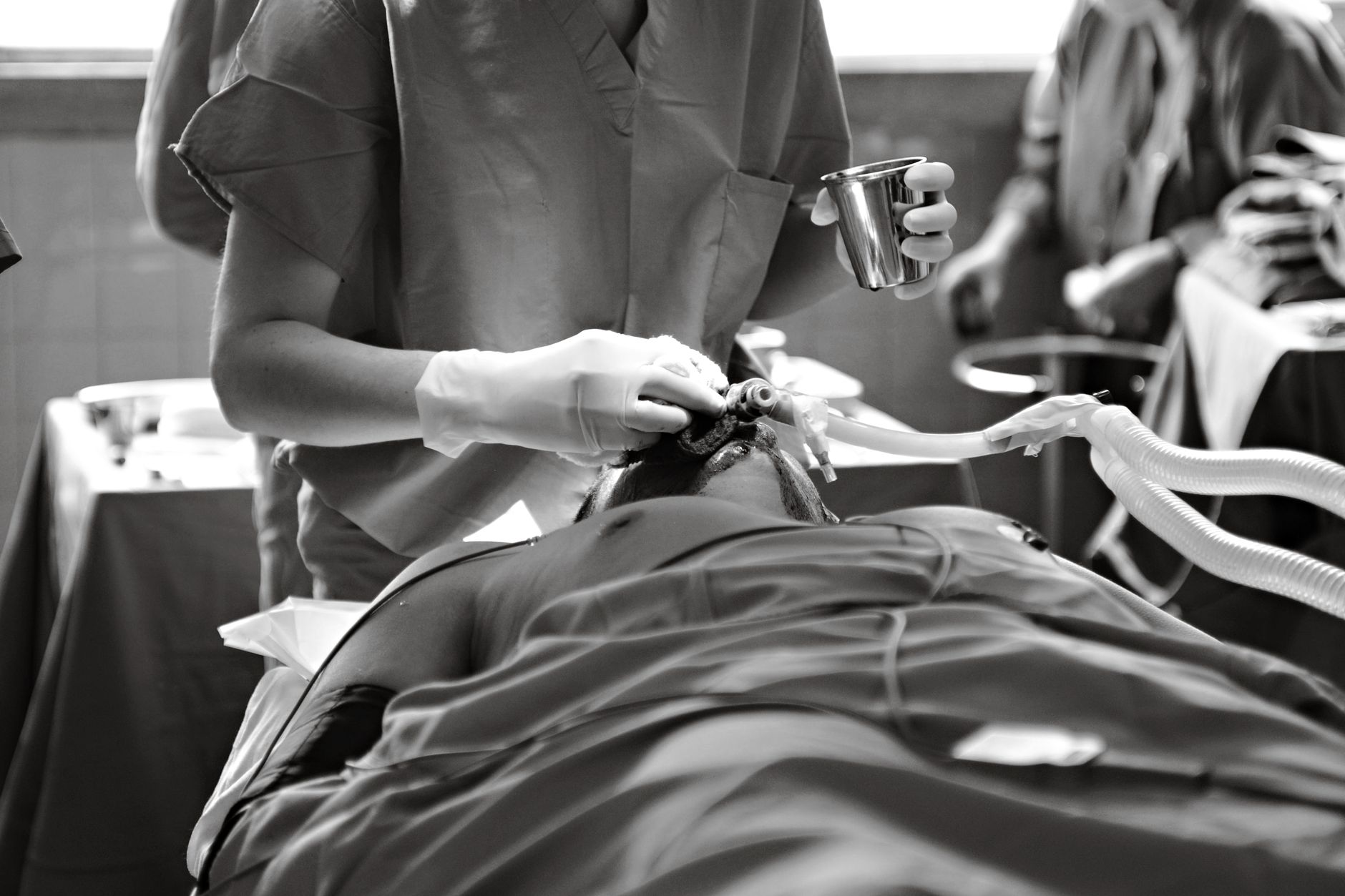 Black and white image of a medical professional performing a procedure in an operating room.