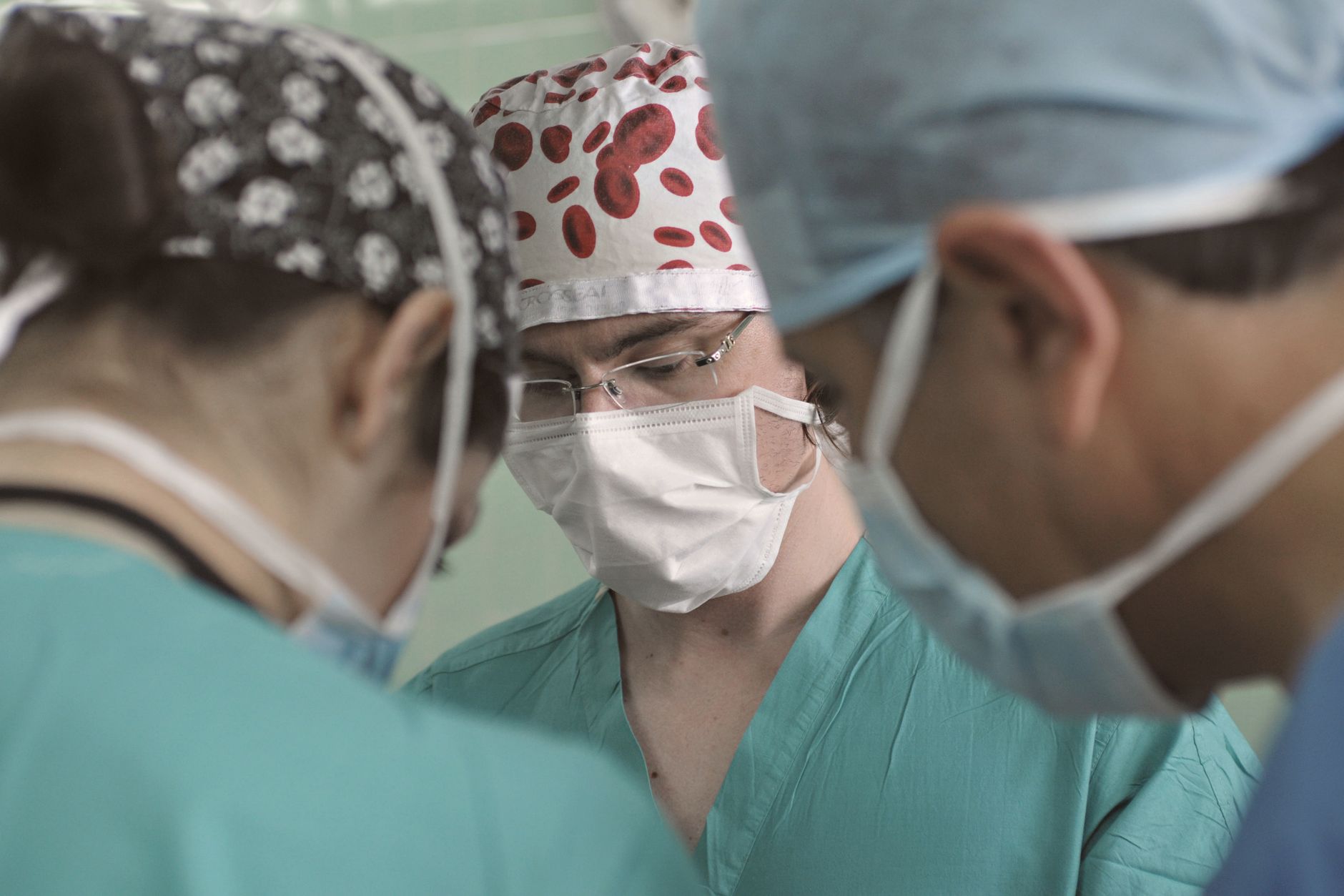 Surgeons wearing masks and scrubs collaborate during a medical operation in an operating room.