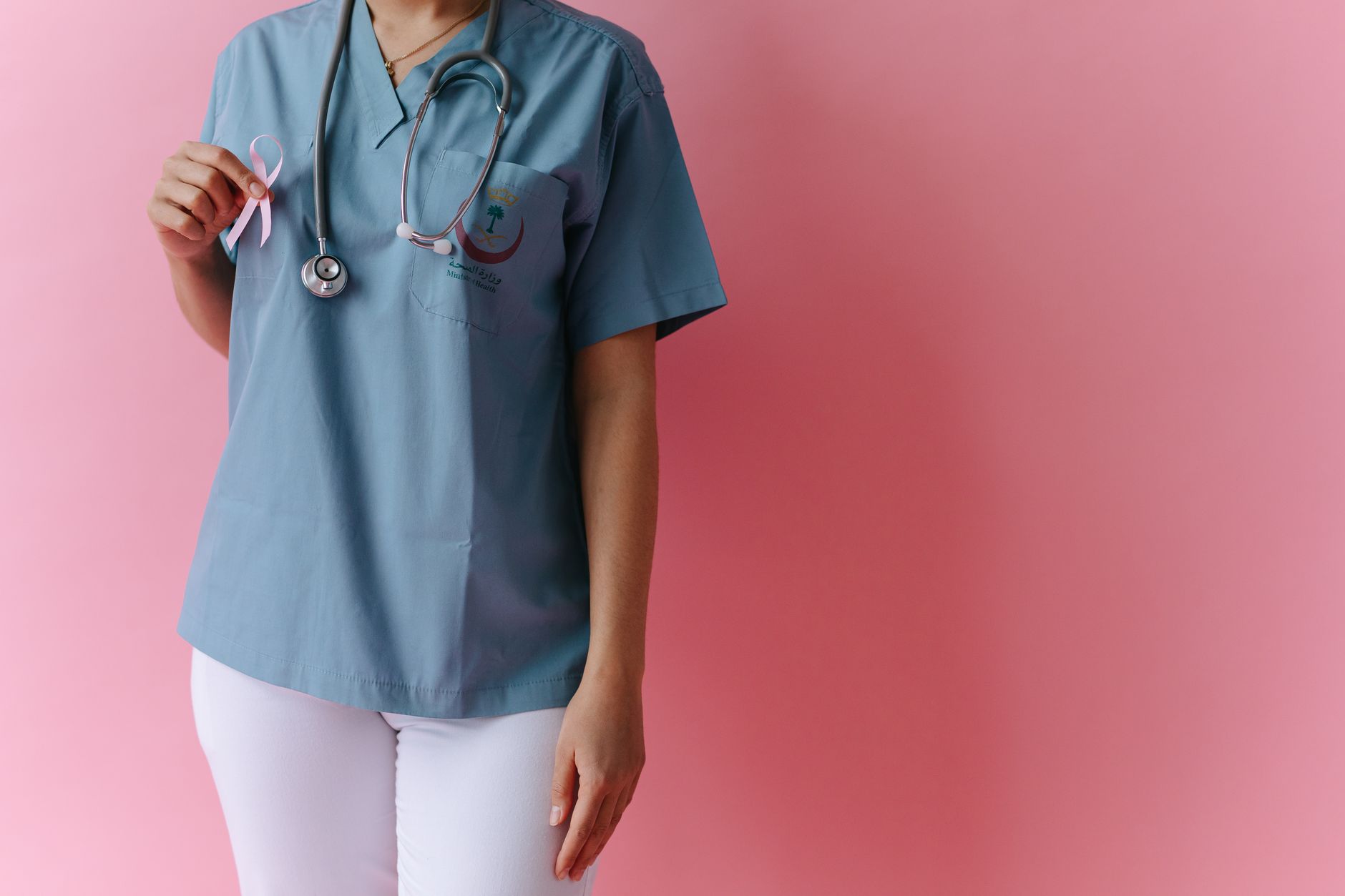 A medical professional holding a pink ribbon for breast cancer awareness against a pink background.