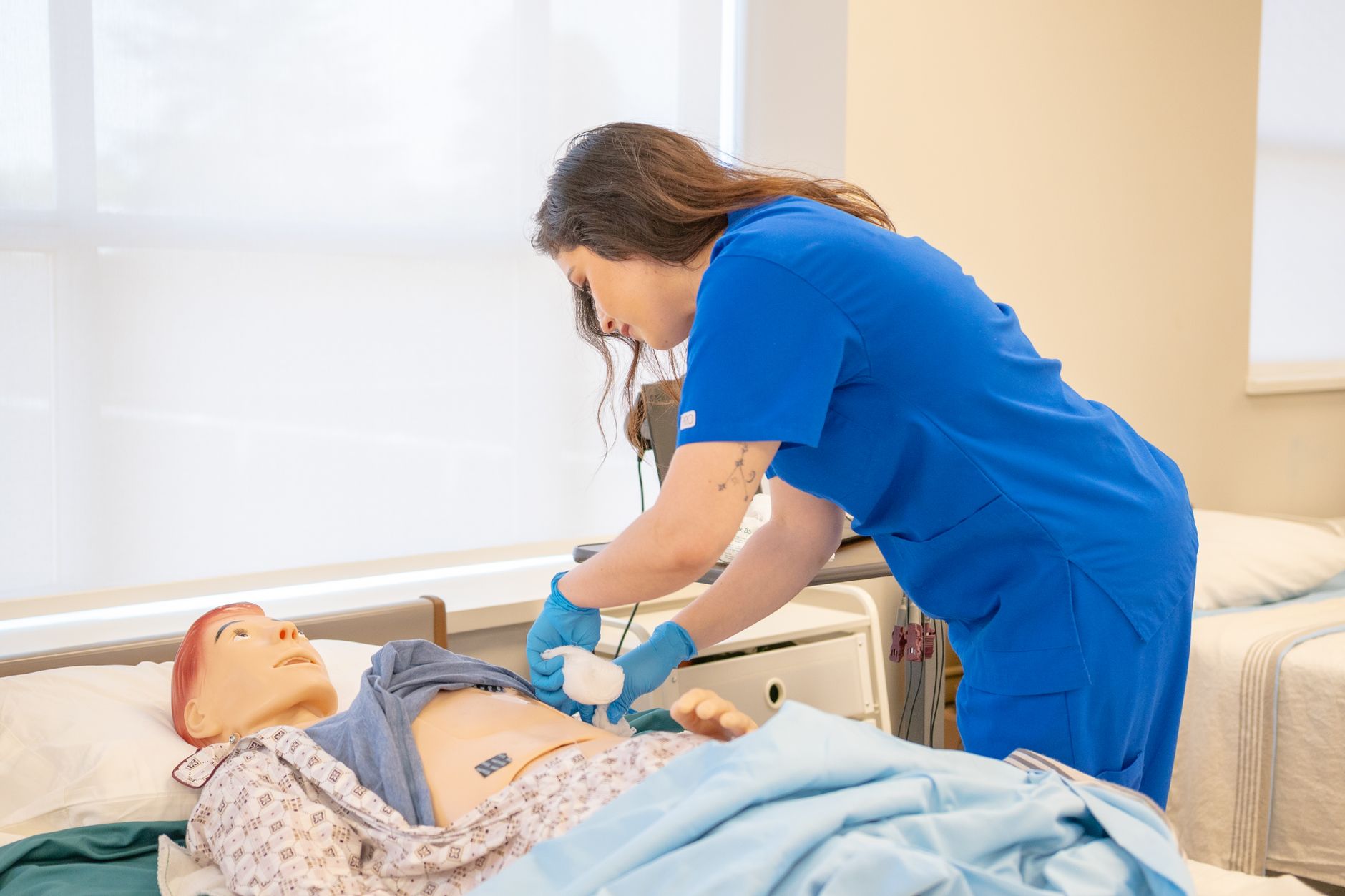 A nurse in blue scrubs practicing medical procedures on a hospital training manikin.